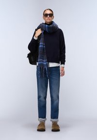 Granatowy sweter, striped turtleneck, niebieski szalik w kratę, jasnoniebieskie dżinsy, brązowe buty i czarna torba. Dodatki to ciemne okulary przeciwsłoneczne.