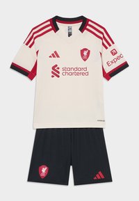 Nogometna oprema Liverpool FC, ki vključuje smetanast dres z rdečimi poudarki, V-izrezom in logotipom, v kombinaciji s črnimi kratkimi hlačami, ki prikazujejo rdeči klubovski grb.