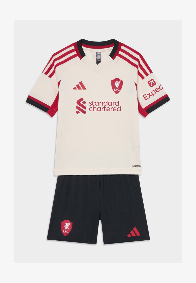 Nogometni dres Liverpool FC-a s kremastom majicom s crvenim detaljima, V-izrezom i logotipom, uparenim s crnim šortsevima koji prikazuju crveni grb kluba.