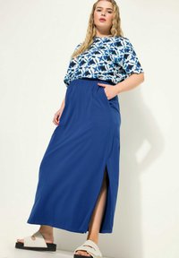 Blauwe maxi-rok met een zijsplits en elastische tailleband, gecombineerd met een kort-gevleugelde, bedrukte top met een geometrisch patroon in blauw en wit.