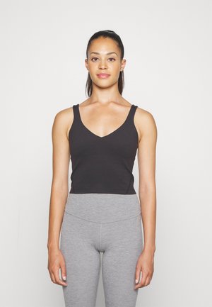 Black cropped tank top with a V-neckline and wide straps, made of a smooth fabric. Paired with high-waisted gray leggings.