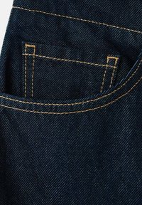 Temno modra denim tkanina z natančnim rumenim šivom, ki obroblja majhen žep znotraj večjega žepa na kavbojkah.