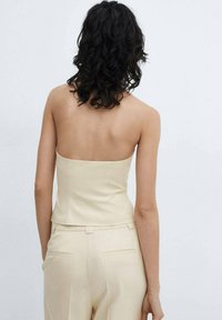 Haut beige sans bretelles, au design ajusté, texture lisse et coutures minimales ; associé à un pantalon beige assorti, de coupe ajustée.