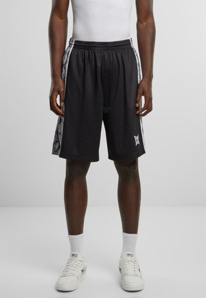 Sorte sports shorts lavet af mesh-materiale. Har et hvidt slange mønster på siderne og en elastisk talje. Bæres med hvide sneakers.