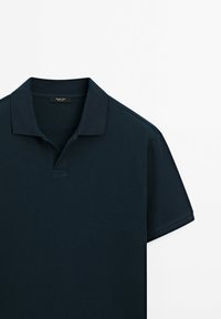 Polo bleu marine à manches courtes avec tissu texturé, col ouvert et étiquette de marque discrète à l'intérieur du col.