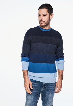 Ronde hals trui met horizontale strepen in marineblauw, donkerblauw en lichtblauw tinten, met geribbelde manchetten en zoom. Zachte gebreide textuur.