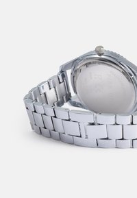 Orologio in acciaio inossidabile argento con cassa tondeggiante, corona visibile e bracciale a maglie lucido. Il fondello trasparente rivela i dettagli interni.