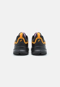 Baskets de sport noires et oranges avec un dessus texturé, un talon rond et des accents roses contrastants sur la languette et le col.