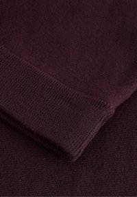 Tessuto di maglione in borgogna con una texture liscia; presenta polsini a coste e un motivo sottile e uniforme in tutto il capo.