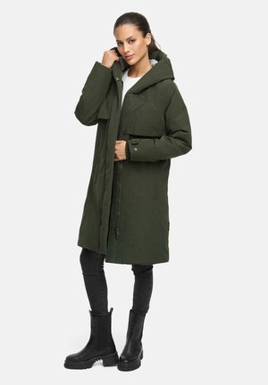 Long manteau parka vert olive avec une capuche, fermeture éclair sur le devant et deux poches poitrine. Assorti avec un pantalon noir ajusté et des bottes noires imposantes.