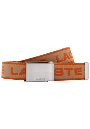 Beige og orange stofbælte med gentagende "LACOSTE" tekst og en sølvmetallås med indgraveret "LACOSTE" logo.