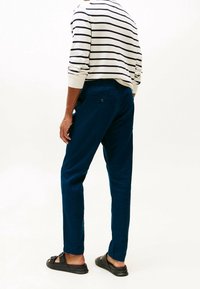 Tmavě modré joggingové kalhoty s elastickým páskem, dvojicí zadních kapes, hladkou texturou a nošené s pruhovaným svetrem a černými sandály.