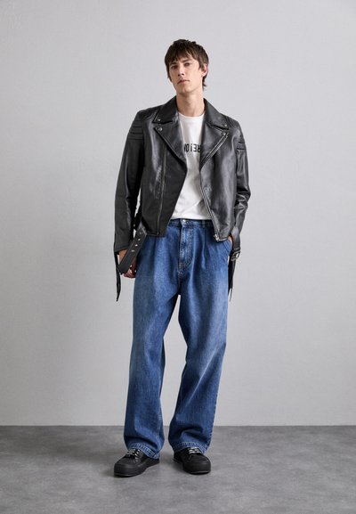 Must värvi nahast mootorratturi jakk hõbedaste detailidega, valge T-särk ja laiad sinised denim püksid, kombineeritud mustade nööriga kingadega.