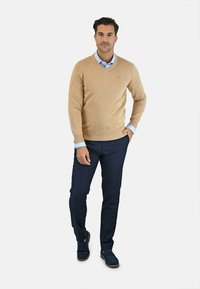 Suéter beige con un diseño de escote en V combinado con pantalones azul marino y zapatos tipo slip-on en azul marino. El conjunto incluye una camisa de color azul claro con cuello debajo.