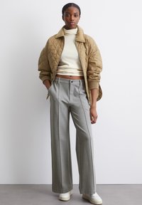 Veste bomber matelassée beige sur un col roulé crème, associée à un pantalon large gris décontracté et des baskets blanches. Textures douces et couleurs pastel.