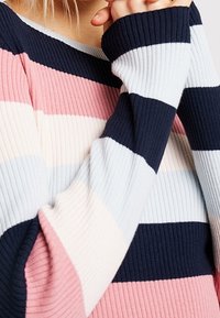 Ribbed sweter z poziomymi paskami w kolorze granatowym, jasnoniebieskim, różowym i białym. Rękawy są długie i mają ściągacze.