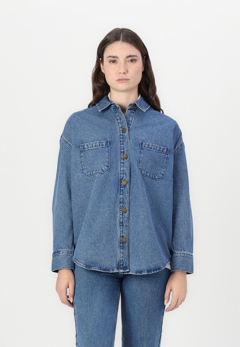 Camicia di denim con chiusura a bottoni frontale, colletto a punta, due tasche sul petto, maniche lunghe e vestibilità rilassata, caratterizzata da tonalità blu e una finitura sbiadita.