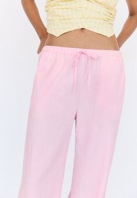 Pantalons larges roses clair avec une taille élastique et un cordon de serrage. Le tissu semble doux avec une texture lisse et une coupe décontractée.