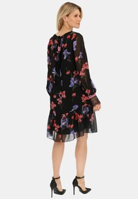 Czarna sukienka w kwiaty z długimi rękawami, ozdobiona czerwonymi i fioletowymi kwiatami, z falbaną u dołu oraz wiązanym dekoltem. Noszona z czarnymi szpilkami z paskiem za kostkę.