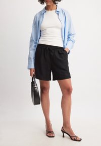 Pantaloni corti neri con vita elasticizzata, abbinati a una canotta bianca e una camicia button-up azzurro chiaro. Borsa nera e scarpe con cinturini.
