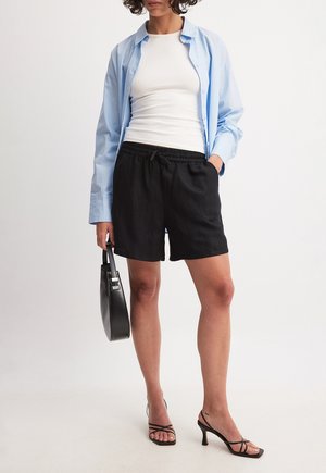 Black shorts with an elastic waistband, paired with a white tank top and a light blue button-up shirt. Black handbag and strappy heels.