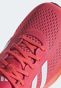 Zapatilla deportiva roja con parte superior de malla transpirable, acentos texturizados, marca blanca en contraste y sistema de cordones seguro.