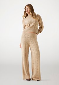 Beige gestrickter Pullover und weite Hosen im Set, mit einem Kabelstrickmuster und gerippten Bündchen. Weiche Textur, figurschmeichelndes Design.