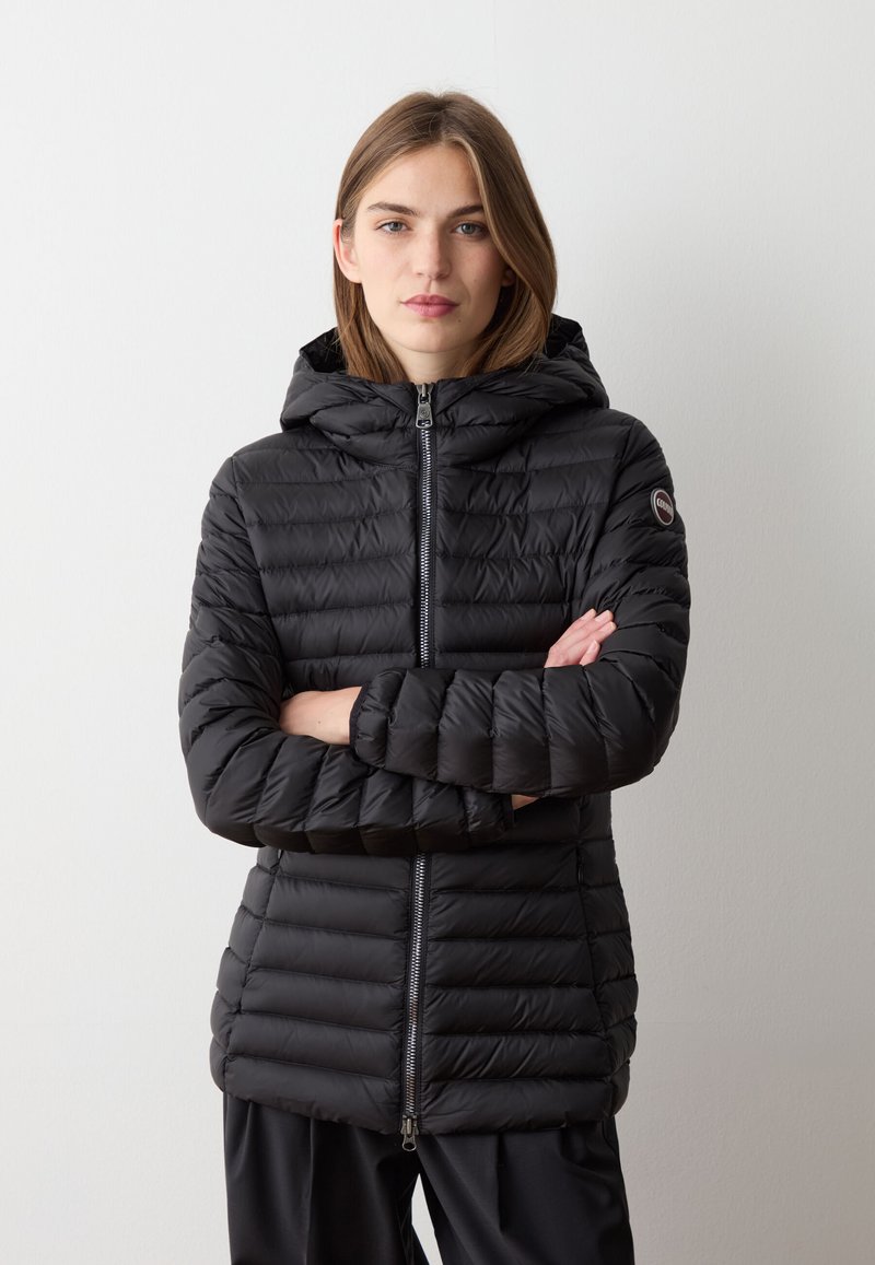 Giacca a vento nera con cappuccio, caratterizzata da una chiusura con zip, design trapuntato e un'etichetta con logo sulla manica sinistra. Realizzata in materiale leggero e liscio.