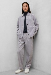 Lys grå kordfløjl jakke og matchende bukser, med en mørk turtleneck nedenunder. Hvide sneakers fuldender outfittet. Minimalistisk design og afslappet pasform.
