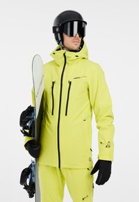 Veste de ski imperméable jaune vif avec une capuche, plusieurs poches zippées et des accents noirs. Comprend des gants noirs et un snowboard.