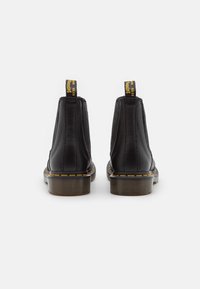 Black leather Chelsea boots with elastic sides, yellow stitching, and a sturdy rubber sole. Features yellow heel pull tabs for easy wear.