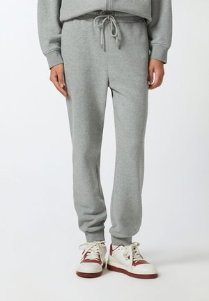Pantaloni grigi in felpa con vita regolabile, caviglie affusolate e una texture morbida. Abbinati a sneakers bianche e bordeaux.