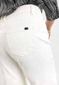 Jeans blancs avec un motif zèbre subtil, dotés d'une poche arrière et d'une étiquette noire. Texture lisse et design ajusté.