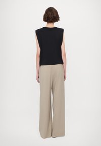 Svart ärmlös topp med en avslappnad passform, i kombination med beigevida byxor i ett mjukt material. Enkel, minimalisk design.