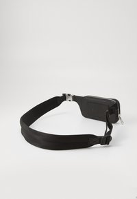 Saco de cintura preto com alça ajustável, apresentando um compartimento com fecho e uma superfície texturizada. Design elegante e minimalista.