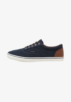 Sneakers z granatową tkaniną na górze, brązowymi skórzanymi akcentami, białą gumową podeszwą, okrągłym noskiem oraz zapinane na sznurówki z pięcioma oczkami.