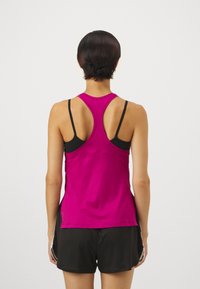 Fuchsia träningslinne med racerbaksdesign, med en mjuk textur och kontrasterande svarta axelremmar. Matchat med svarta shorts.
