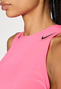 Rosa ärmelloses Nike Sporttop mit glatter Textur, gerundetem Ausschnitt und schwarzen Logoakzenten nahe den Schulternähten.