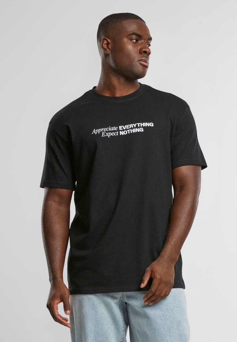 Black cotton t-shirt with short sleeves, crew neck, featuring white text that reads "Appreciate EVERYTHING Expect NOTHING."