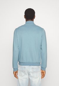 Sudadera azul claro con un cuello alto y puños acanalados, hecha de una tela suave. Presenta un corte relajado y un dobladillo. Diseño minimalista.