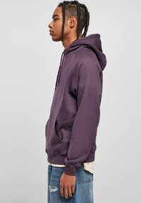 Paarse hoodie van zacht materiaal, met een voorzak en een capuchon met trekkoord. Gekocht bij versleten spijkerbroek.