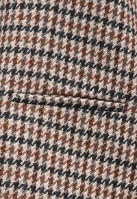 Tecido em mistura de lã com padrão de pied-de-poule em tons de preto, branco e laranja-escuro; apresenta um discreto detalhe de bolso.