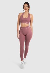 Zestaw sportowy w kolorze mauve, składający się z topu na krótko oraz legginsów z wysokim stanem. Charakteryzuje się dopasowanym krojem i miękką teksturą. Ozdobiony logo "SMIL".