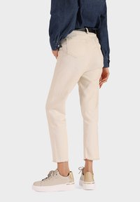 Jeans accorciati color crema con orlo sfrangiato. Abbinati a sneakers beige con dettagli riflettenti. Camicia di denim in blu navy.