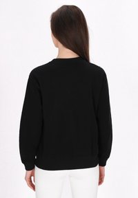 Fekete hosszú ujjú pulóver kerek nyakkivágással. Puha anyag, bordás mandzsetták és szegély, valamint laza szabás. Fehér nadrág van alatta.