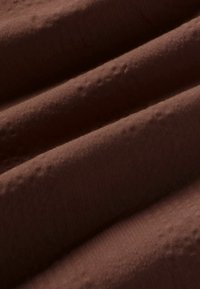 Gros plan d’un tissu doux brun foncé avec une texture subtile et des plis créant des ombres et des reflets diagonaux.