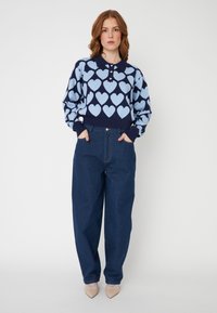Suéter navy com padrão de corações azul claro, gola com colarinho e três botões; combinado com jeans escuros de cintura alta e folgados.