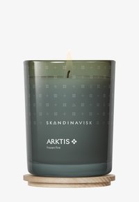 Vela aromática Skandinavisk Arktis de color verde oscuro encendida, con sutiles símbolos nórdicos en el cristal, reposando sobre un posavasos redondo de madera.
