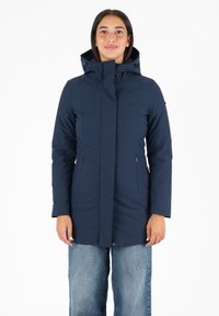 La veste imperméable bleu marine présente un col haut, une capuche amovible et des poches zippées sur le devant, avec une coupe ajustée et une texture lisse.