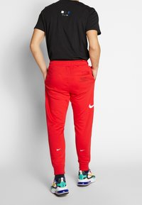 Röda joggers med elastisk midja och sidofickor; har en vit Nike-logga och textdetalj på baksidan. Svart T-shirt med färgade detaljer.
